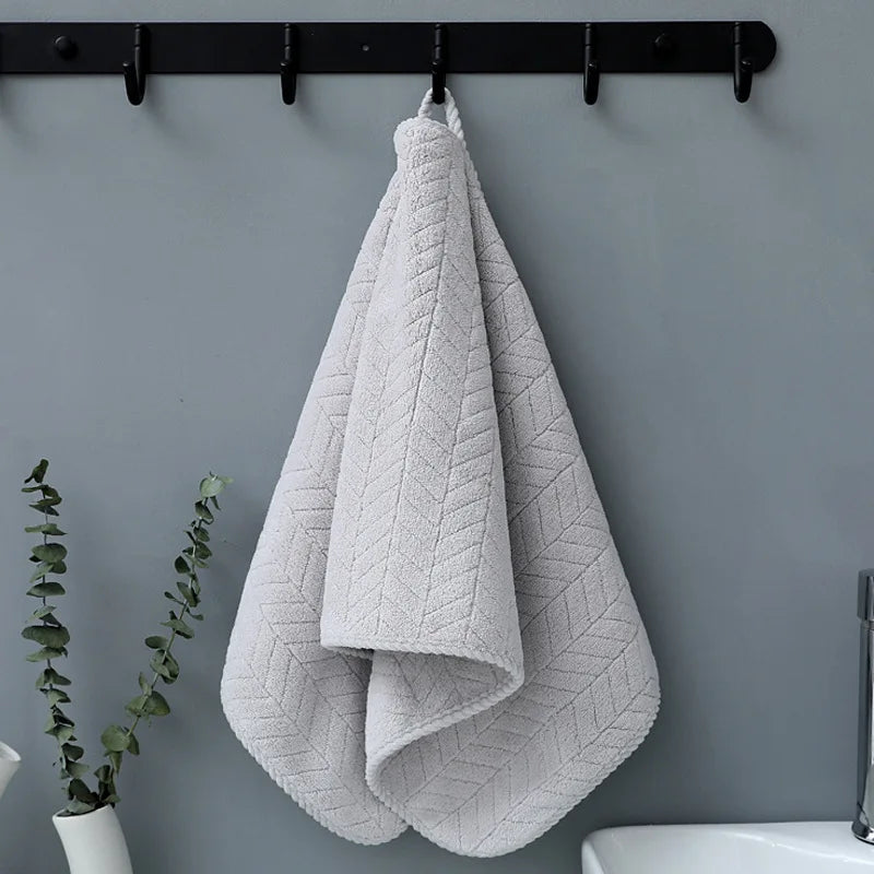 A folded light gray plush microfiber bath towel hanging on a black rack against a gray wall.