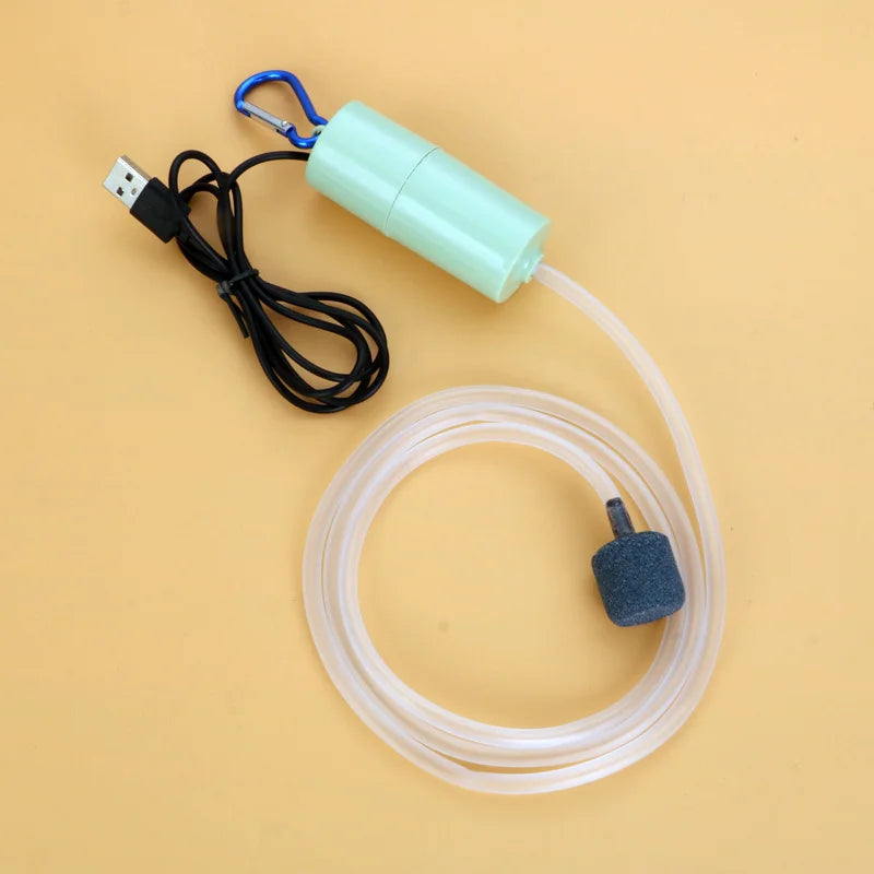 A light green USB silent air pump with a blue clip and clear tubing is shown on a beige background.