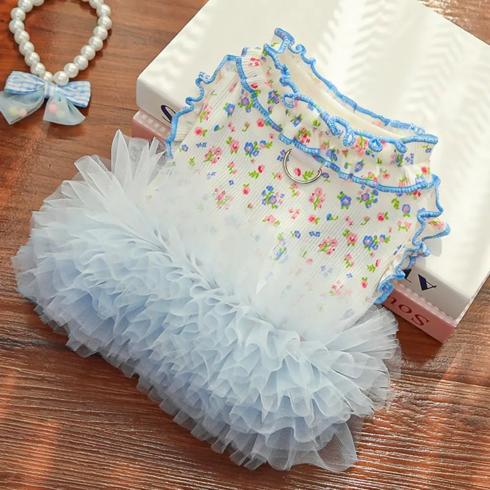 A light blue floral vest for dogs and cats displayed on a wooden surface next to a white box.