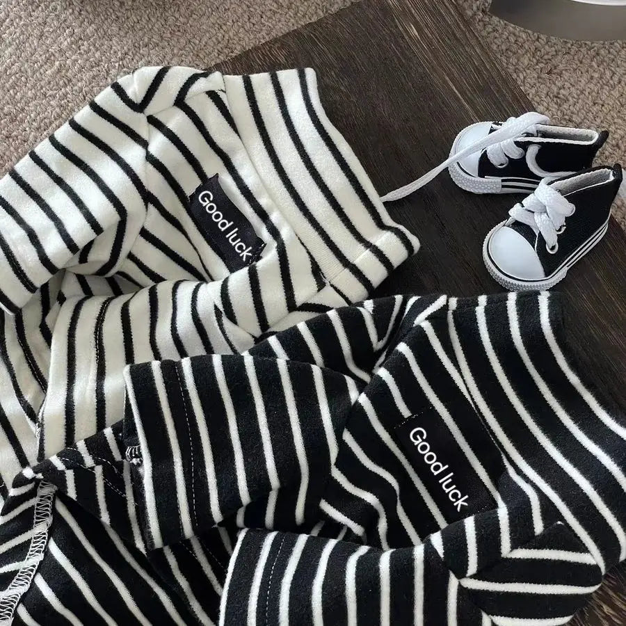 Black and white striped thermal sweater for a small dog lying on a wooden surface.