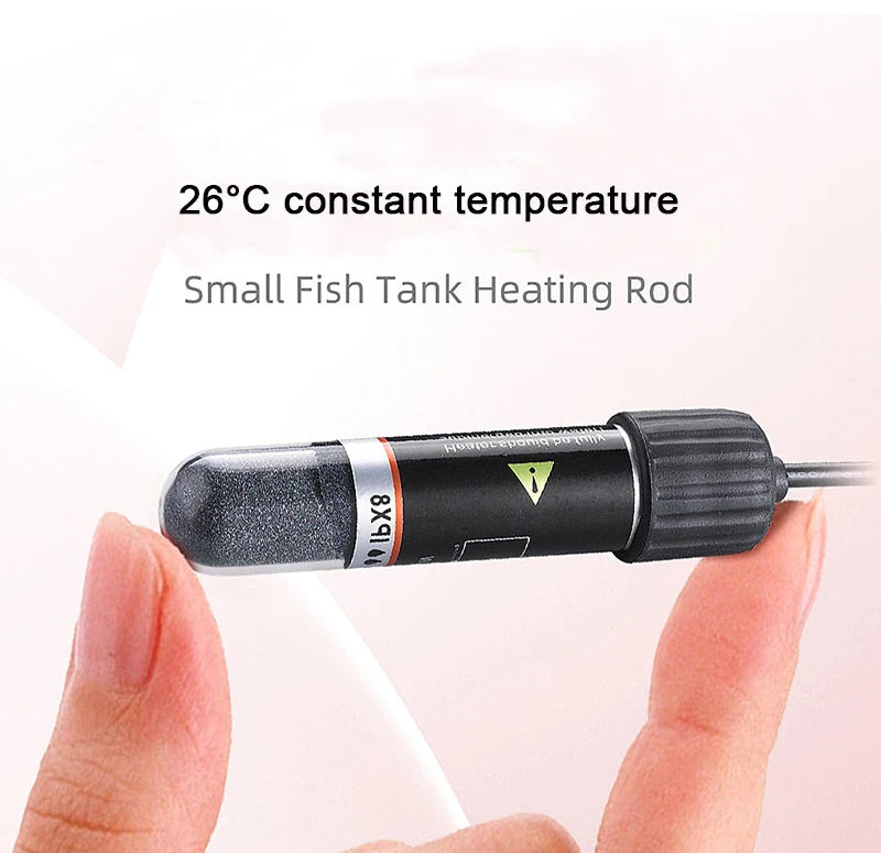 A hand holds a small black heating rod for a fish tank, labeled IBx8, used to maintain a 26°C constant temperature.