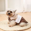 A small, fluffy dog is wearing a beige and brown padded windproof vest with a D-ring on a woven mat.