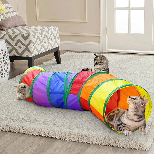 A colorful, foldable interactive cat tunnel toy lying on a light rug with several cats playing.