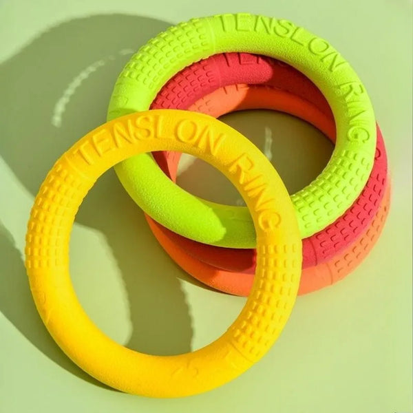 Three brightly colored floating TPR dog flying discs arranged in a circle on a light green surface.