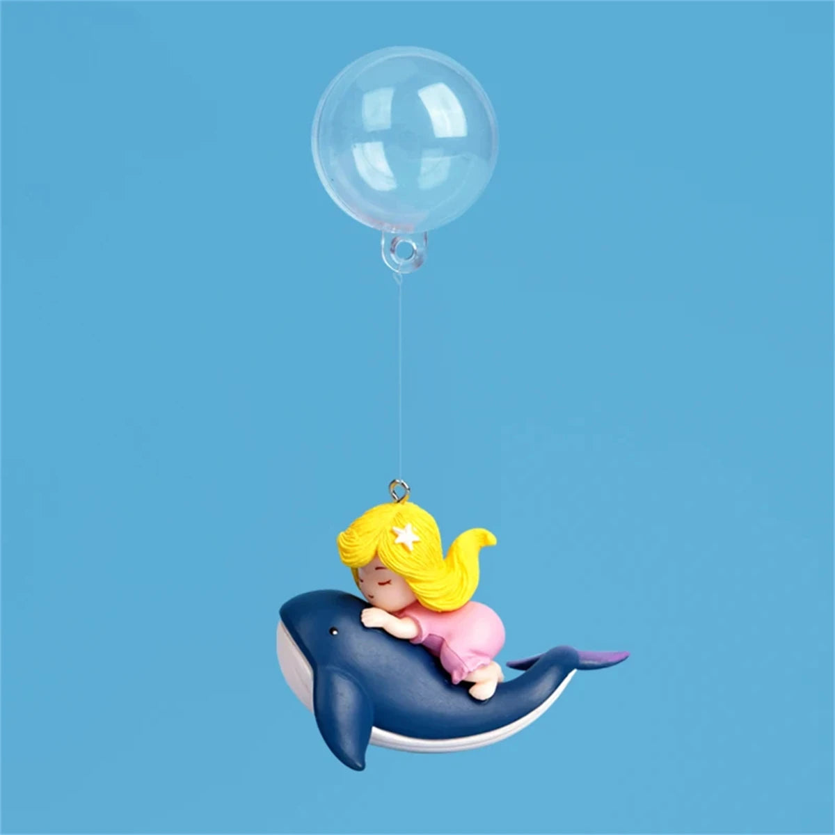 A yellow mermaid figure is floating on a blue dolphin, suspended by a transparent line from a clear balloon.