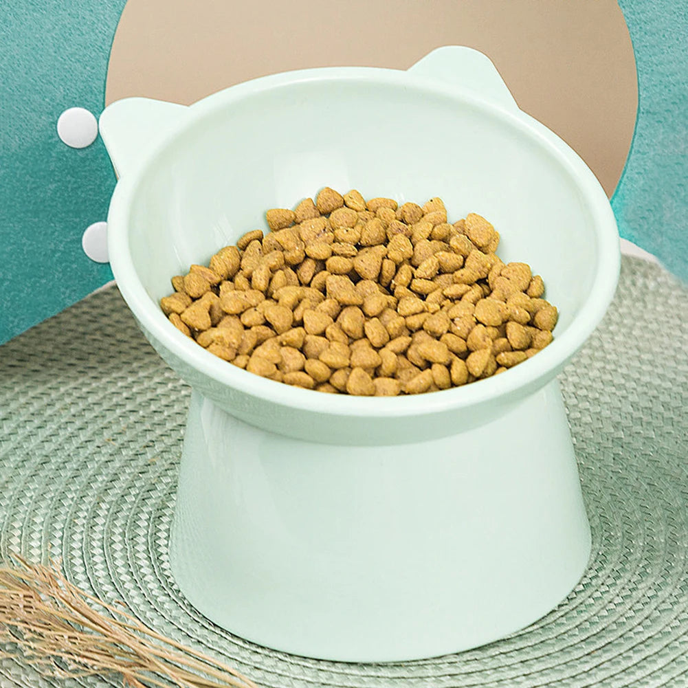 A white ergonomic tilted cat food bowl with a non-slip base filled with dry kibble.