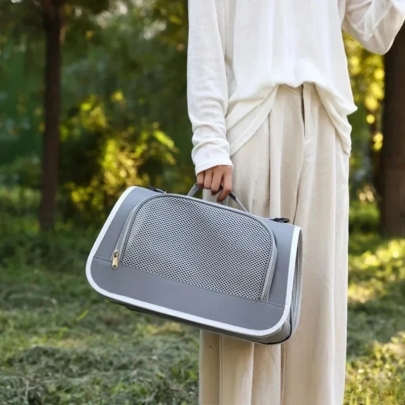 A person holds a gray breathable pet carrier bag for cats and small dogs outdoors.