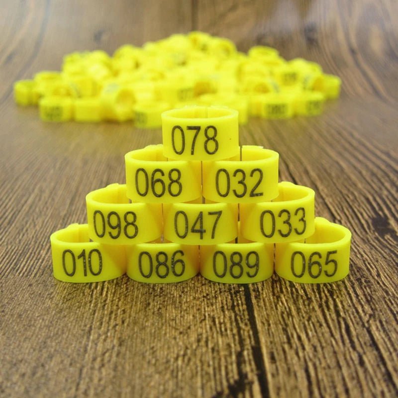 A pile of yellow plastic bird identification foot rings, numbered 010 through 089, resting on a wooden surface.