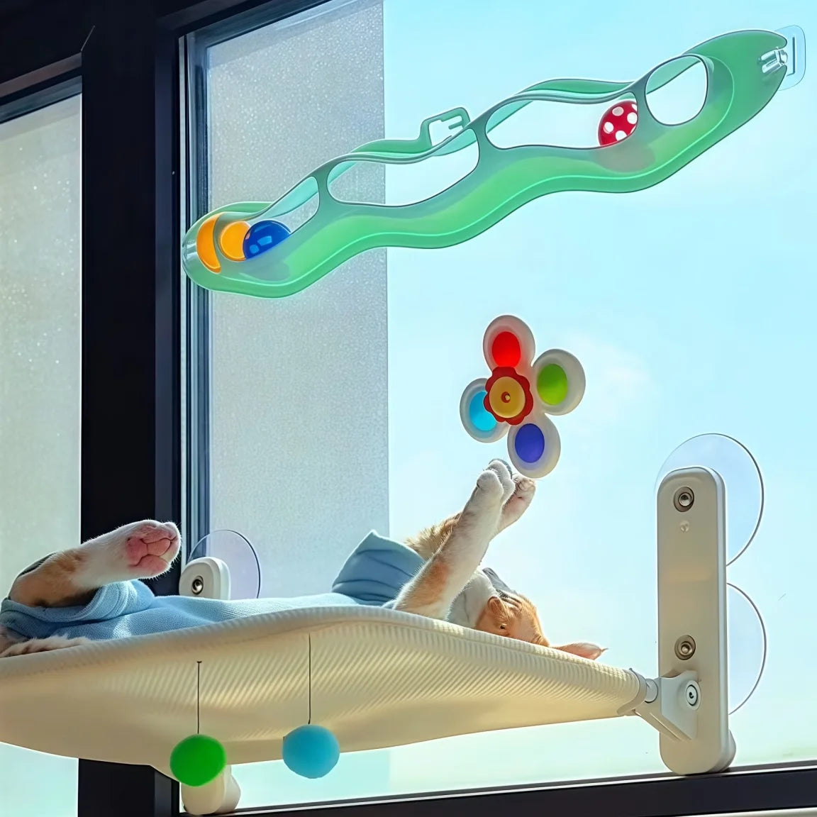 Un jeu de bain pour chat en plastique vert avec des balles colorées, suspendu devant une fenêtre.