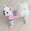 A white dog wearing a pink basketball vest with black lettering lying on a wooden floor.