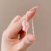 A hand holds a pink elastic hair tie with a cute cartoon design against a neutral background.