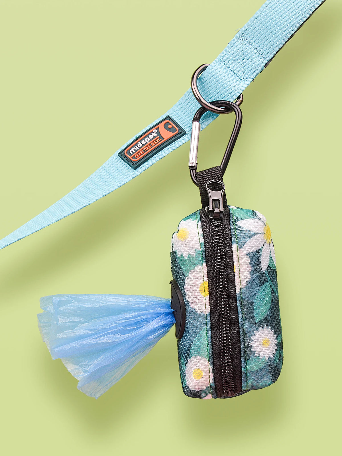 A teal leash clip dispenser with a zippered pouch and a blue fabric flap is shown against a light green background.