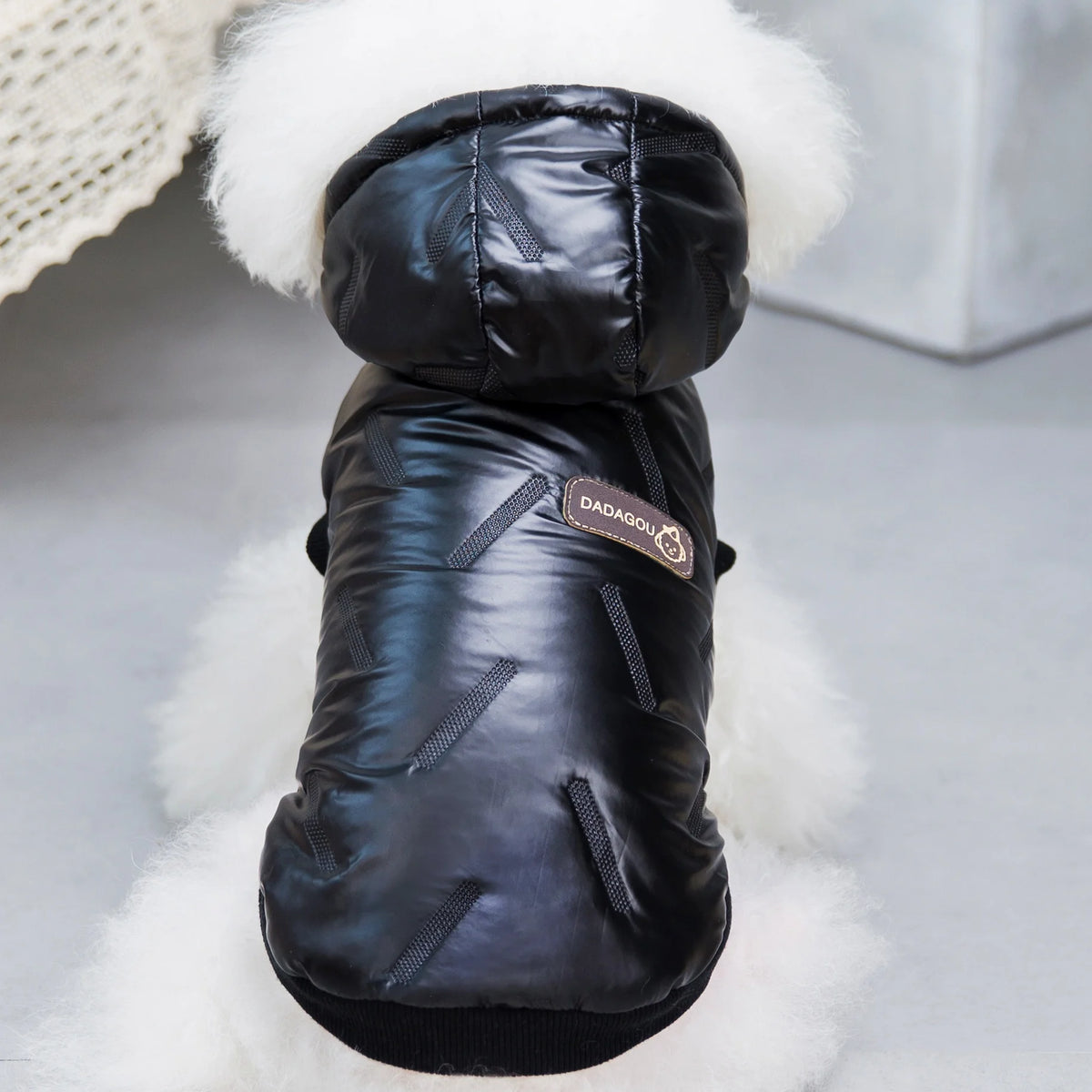A black, quilted dog coat overalls with a white fluffy hood displayed against a light background.