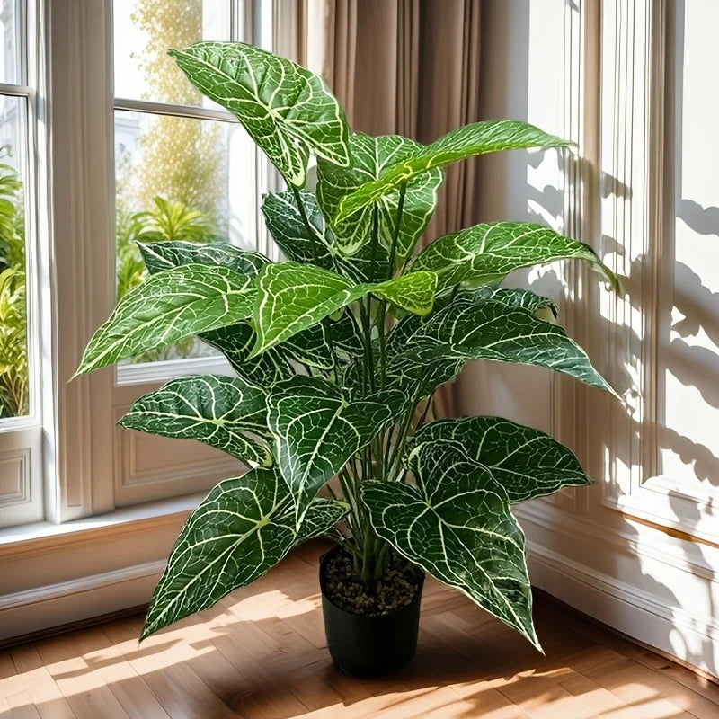 A large, vibrant green artificial monstera plant with deeply lobed leaves sits in a pot next to a window.