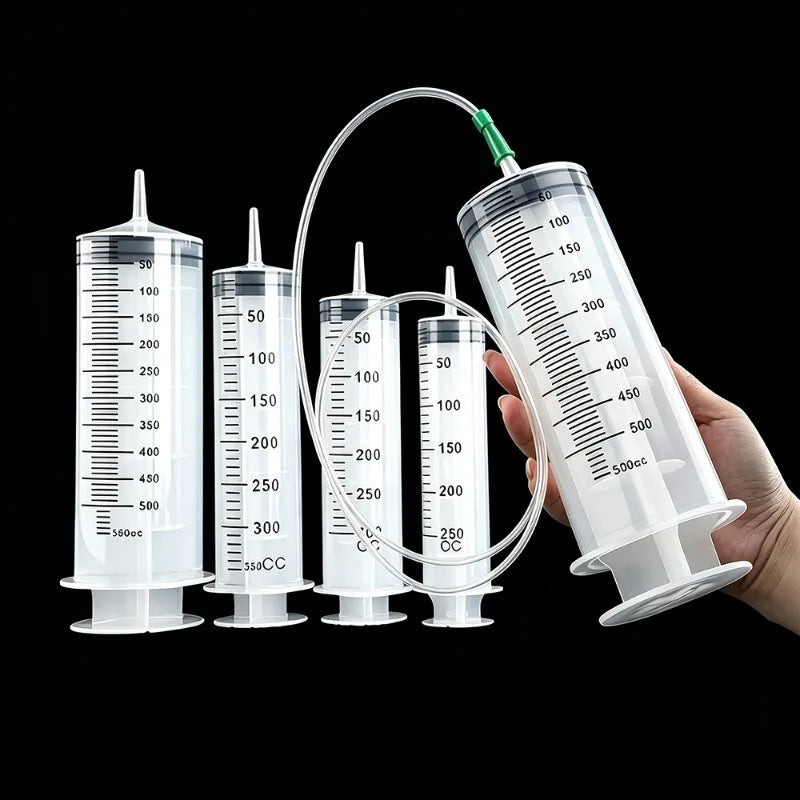 Eine Hand hält eine robuste Plastik-Spritze mit einem flexiblen Schlauch, neben mehreren Messspritzen zur Ölextraktion.