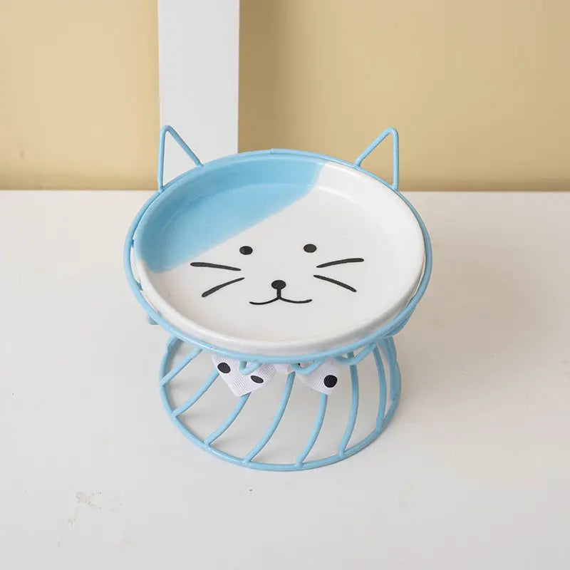 A light blue ceramic cat food dish with a white cat face design sits on a wire stand.