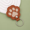 A brown leather paw print keepsake with a silver ring attached, resting on a light green surface.