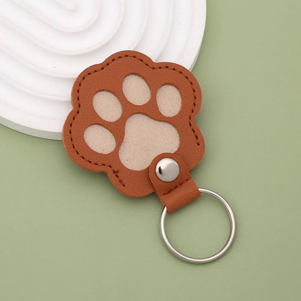 A brown leather paw print keepsake with a silver ring attached, resting on a light green surface.