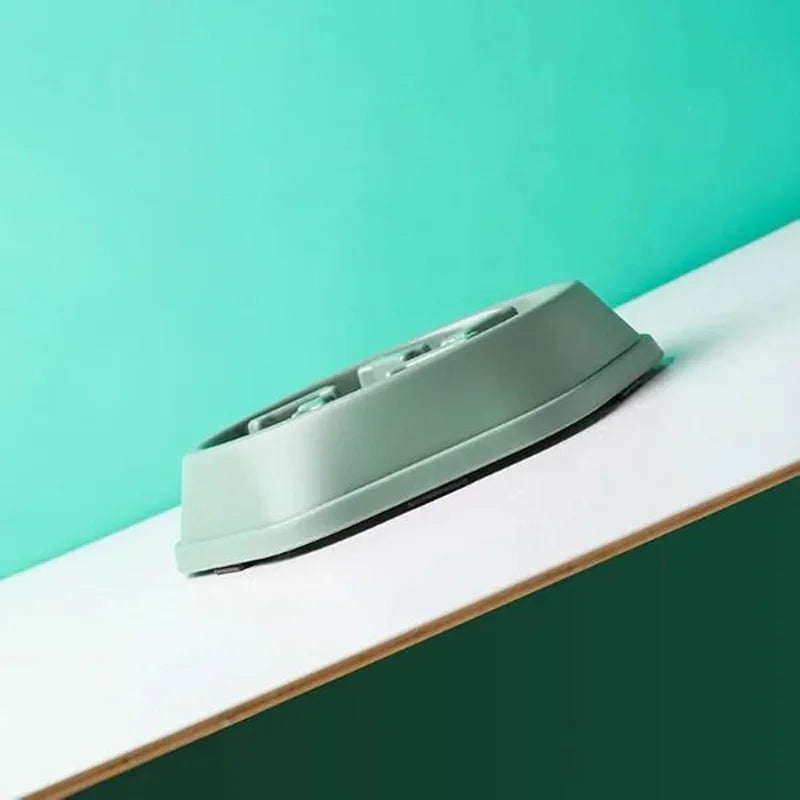A gray slow feeder dog bowl with an anti-slip base resting on a white surface against a teal background.