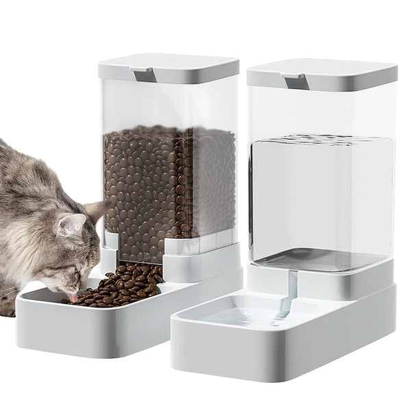 A clear automatic gravity pet feeder and water dispenser unit with a cat feeding from the food compartment.