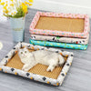 A white cat is lying on a rectangular pet bed with a woven mat and a decorative border, set against a gray background.