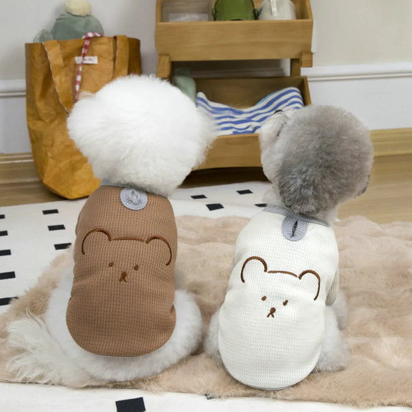 A light beige waffle knit dog shirt with bear embroidery lying on a fluffy rug.