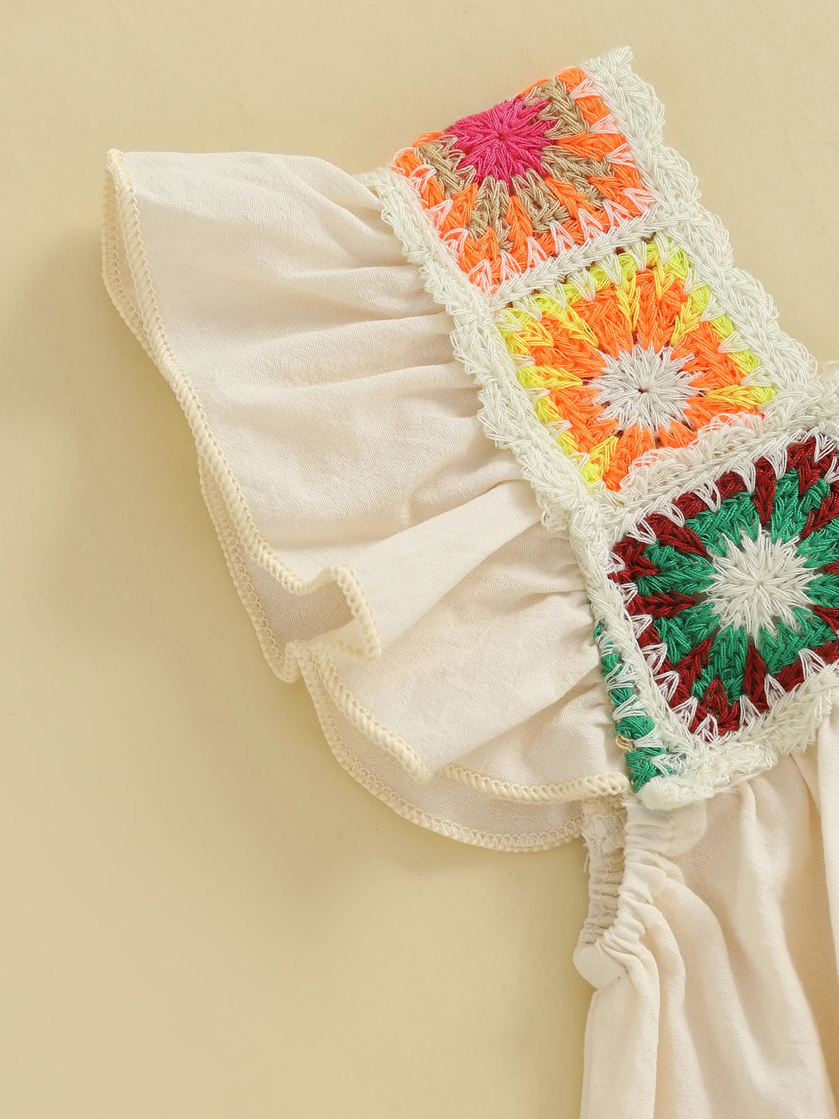 A close-up of a cream-colored toddler romper featuring colorful floral embroidery on the shoulder and sleeve.