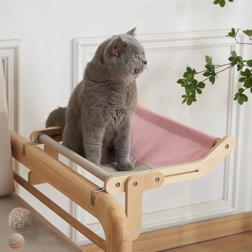 A gray cat sits on a wooden window perch designed for climbing and observation.