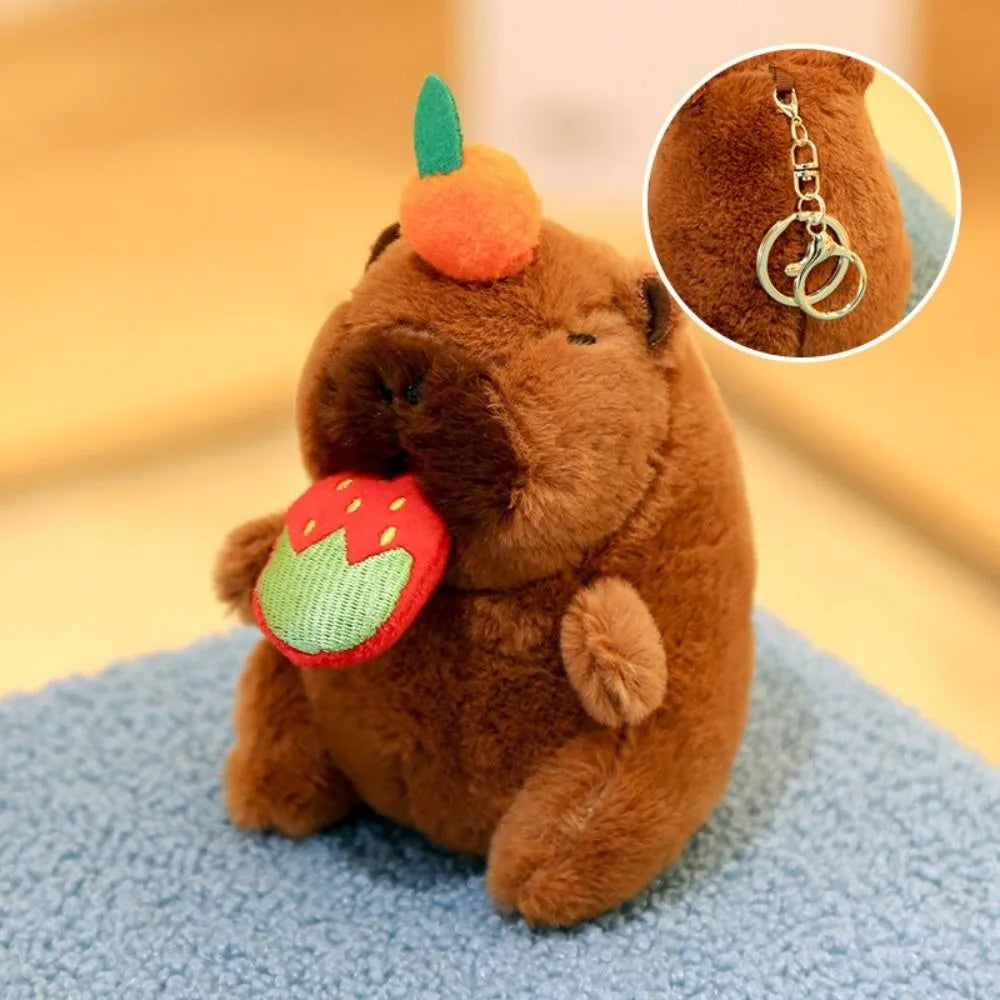 Braunes Capybara-Plüschtier mit orangefarbener Ohrmuschel und grünem Blatt-Accessoire neben einer Nahaufnahme seiner Goldkett