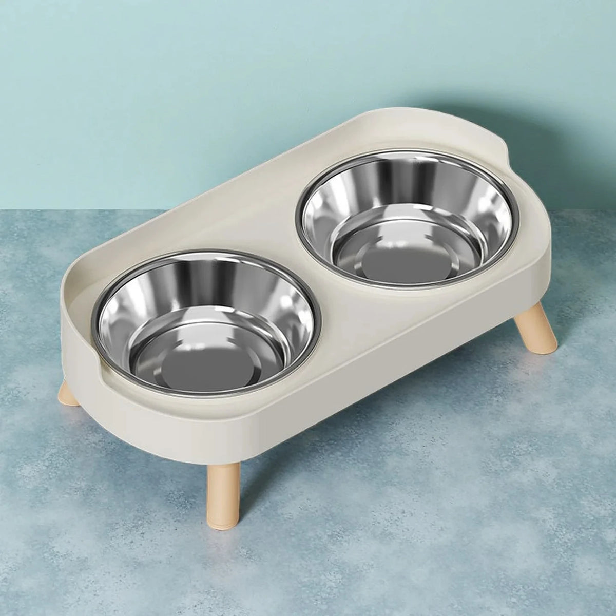 A light beige elevated pet feeder with two stainless steel bowls sits on a wooden stand.