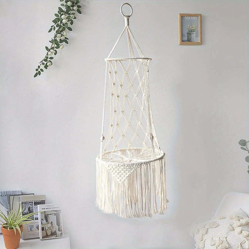 A white macrame cat hammock bed hanging on a wall, featuring woven netting and fringe details.