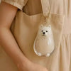 Clé-pendant en figurine de chien blanc, rond et clair, suspendu à une sangle d'un sac en toile beige.