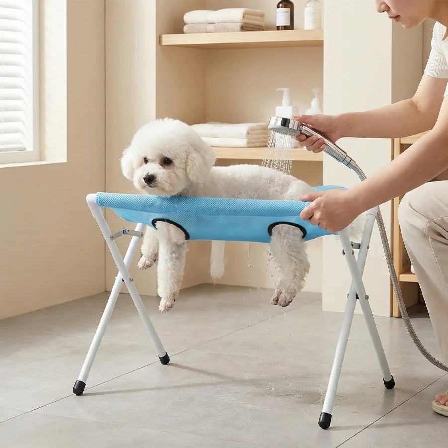 A person is using a foldable pet bathing stand to wash a white poodle.