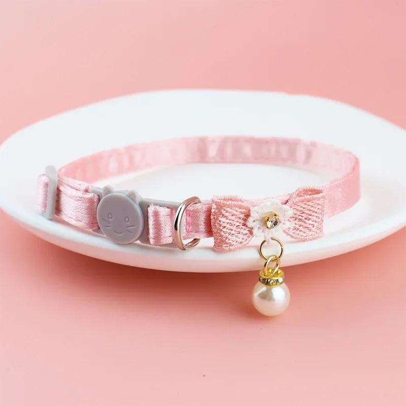 Pink lace bow cat collar with a bell and pearl bead charm displayed on a white plate.