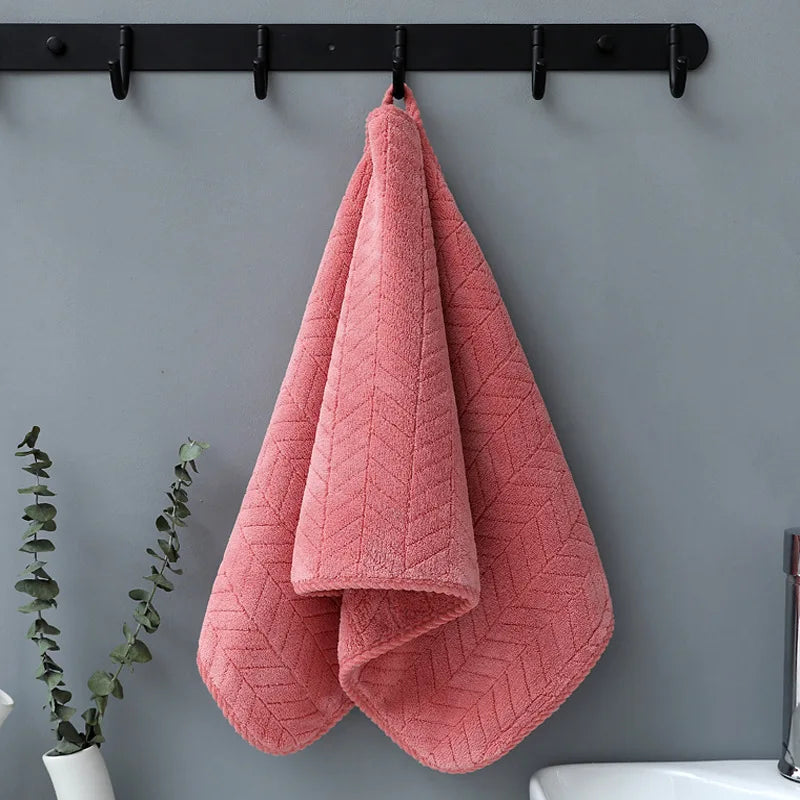 A folded coral pink plush microfiber bath towel hanging on a black rack against a gray wall.