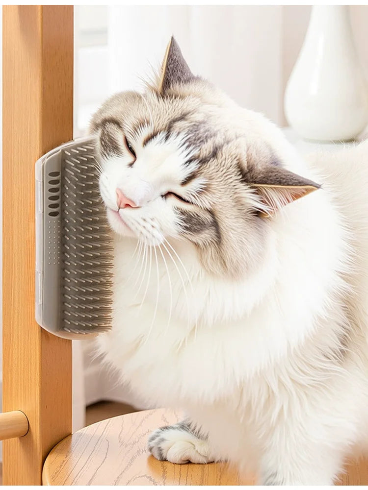 A white and gray cat is relaxing with a silicone grooming brush on a wooden surface.