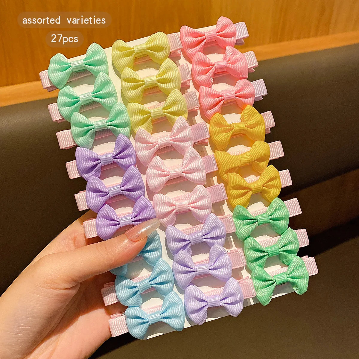An assortment of 27 colorful fabric hair clips in various shades of pink, green, yellow, and purple are displayed on a white 