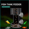 A clear suspended fish tank feeder with multiple small orange pellets and several small fish visible.
