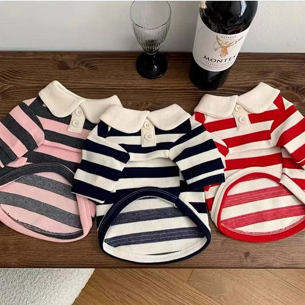 Three striped knitted vests for dogs in pink, navy, and red colors displayed on a wooden surface.