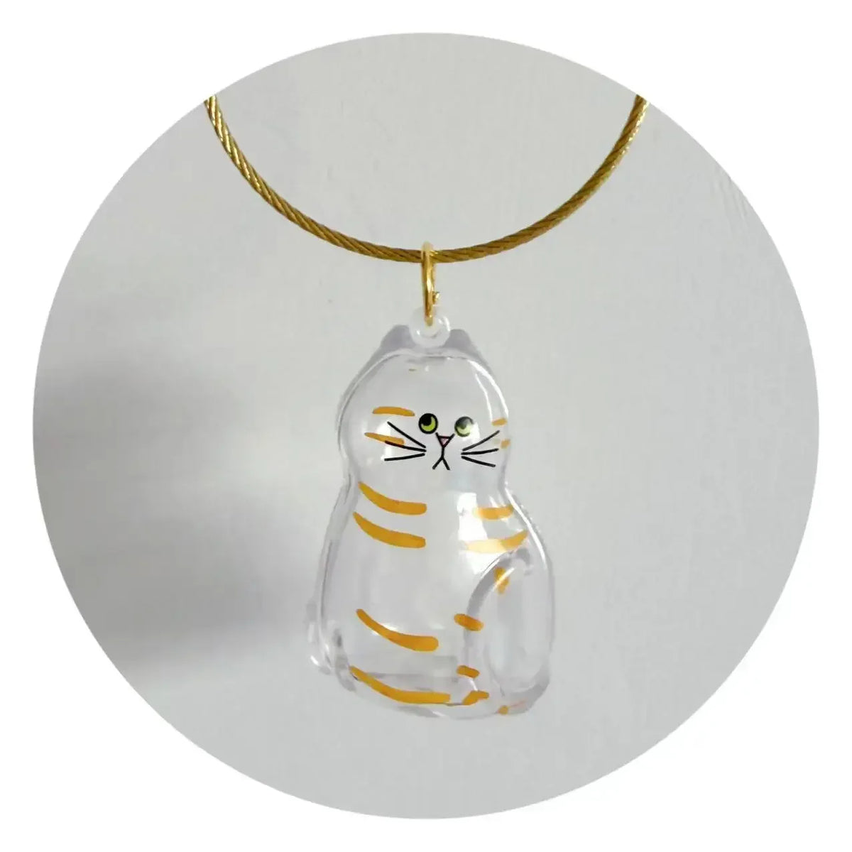 A clear glass charm shaped like a striped cat is suspended from a gold-colored cord.
