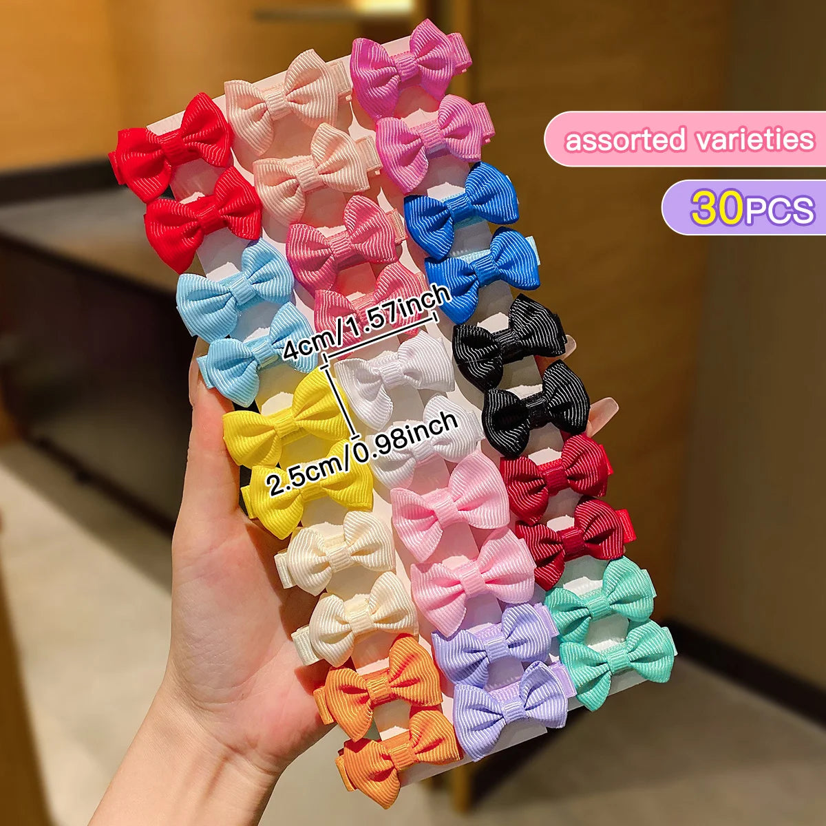 A hand holds an assorted variety of pink, red, blue, and yellow fabric hair clips for children.