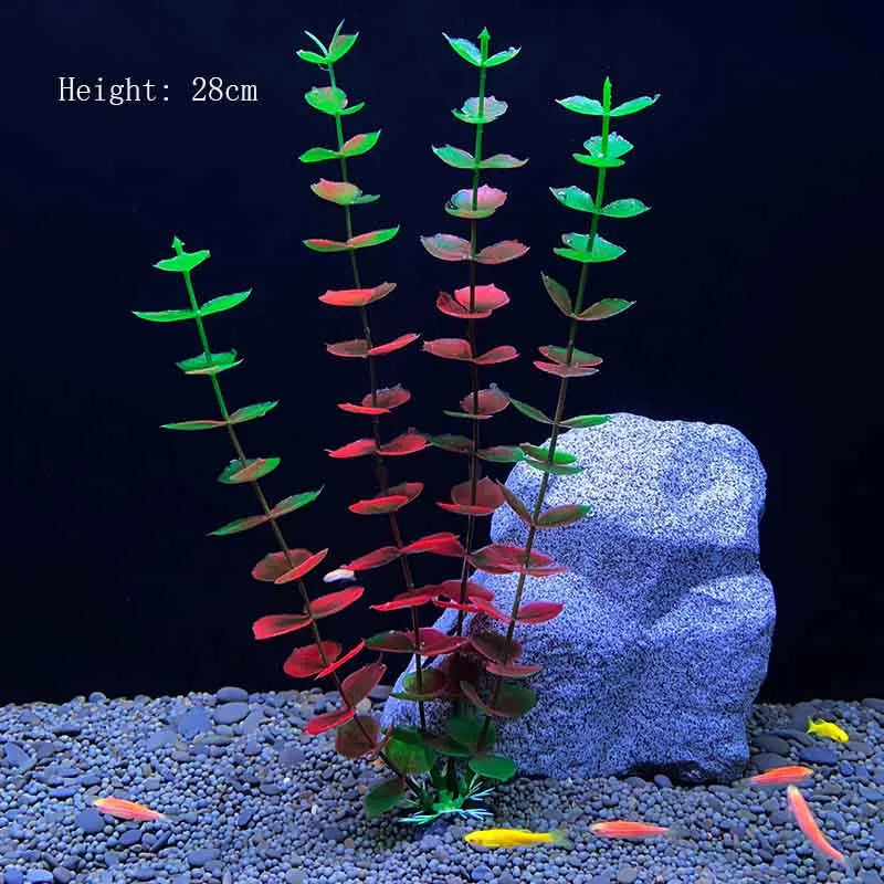 A tall artificial aquarium plant with red and green leaves is displayed on a gray gravel surface next to a large rock.