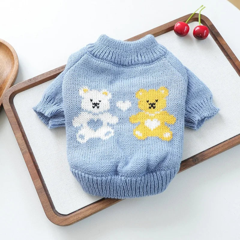 Light blue knitted bear sweater with white and yellow embroidery displayed on a wooden board.