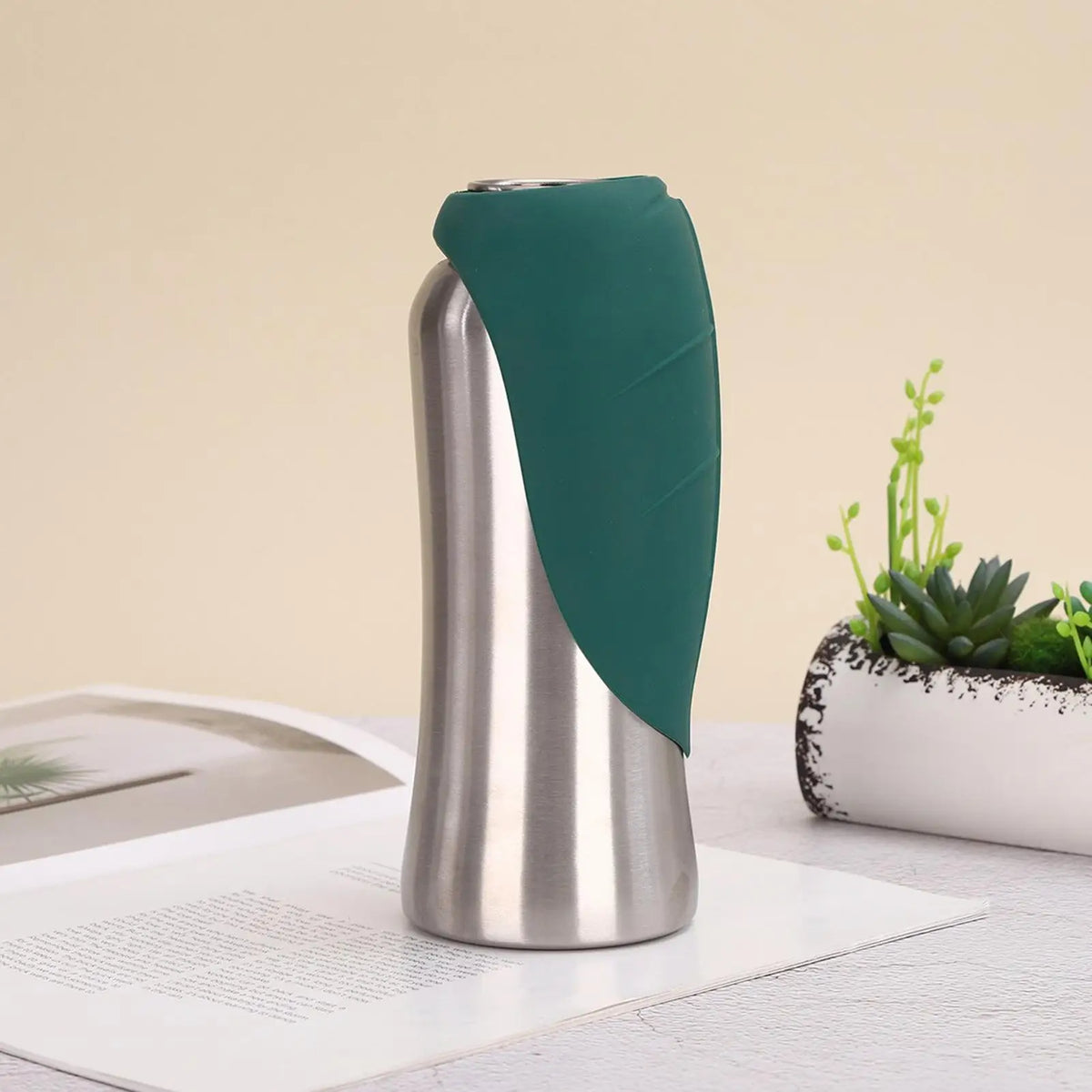 A silver portable dog water bottle with a teal built-in bowl is shown on a white surface.