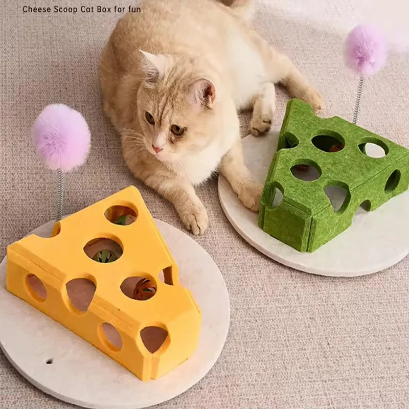 A fluffy orange cat is interacting with a green felt maze play box and a yellow felt cheese scoop toy.