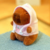 Braune Capybara-Plüschpuppe mit pinkem Hoodie und weißen Zierleisten, sitzt auf blauer strukturierter Oberfläche.