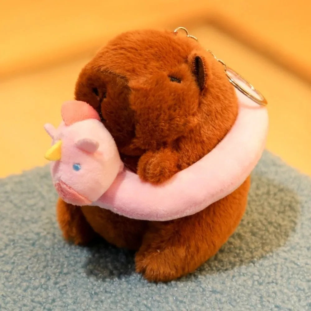 Braune Capybara-Plüschpuppe mit rosa Hoodie und Flügel auf blauem Stoff