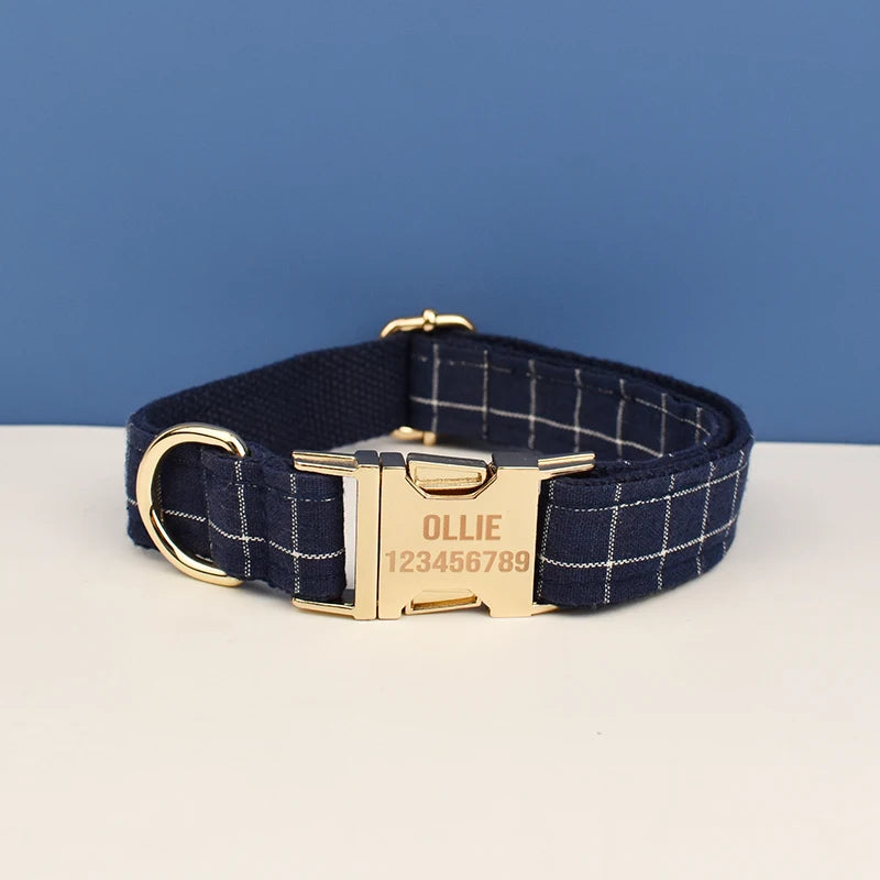 A navy blue plaid dog collar with a gold buckle and the name OLLIE engraved on the tag.