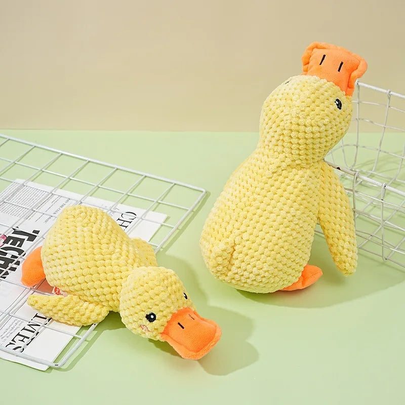 A yellow plush toy shaped like a duck with orange accents, resting on a mesh wire and paper.