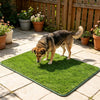 A dog is sniffing a green artificial grass mat placed on a stone patio.